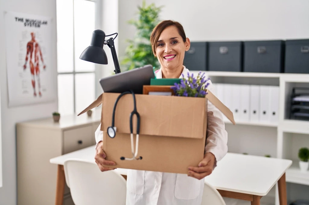 Female physician holding a box of her belongings, moving out of her office.