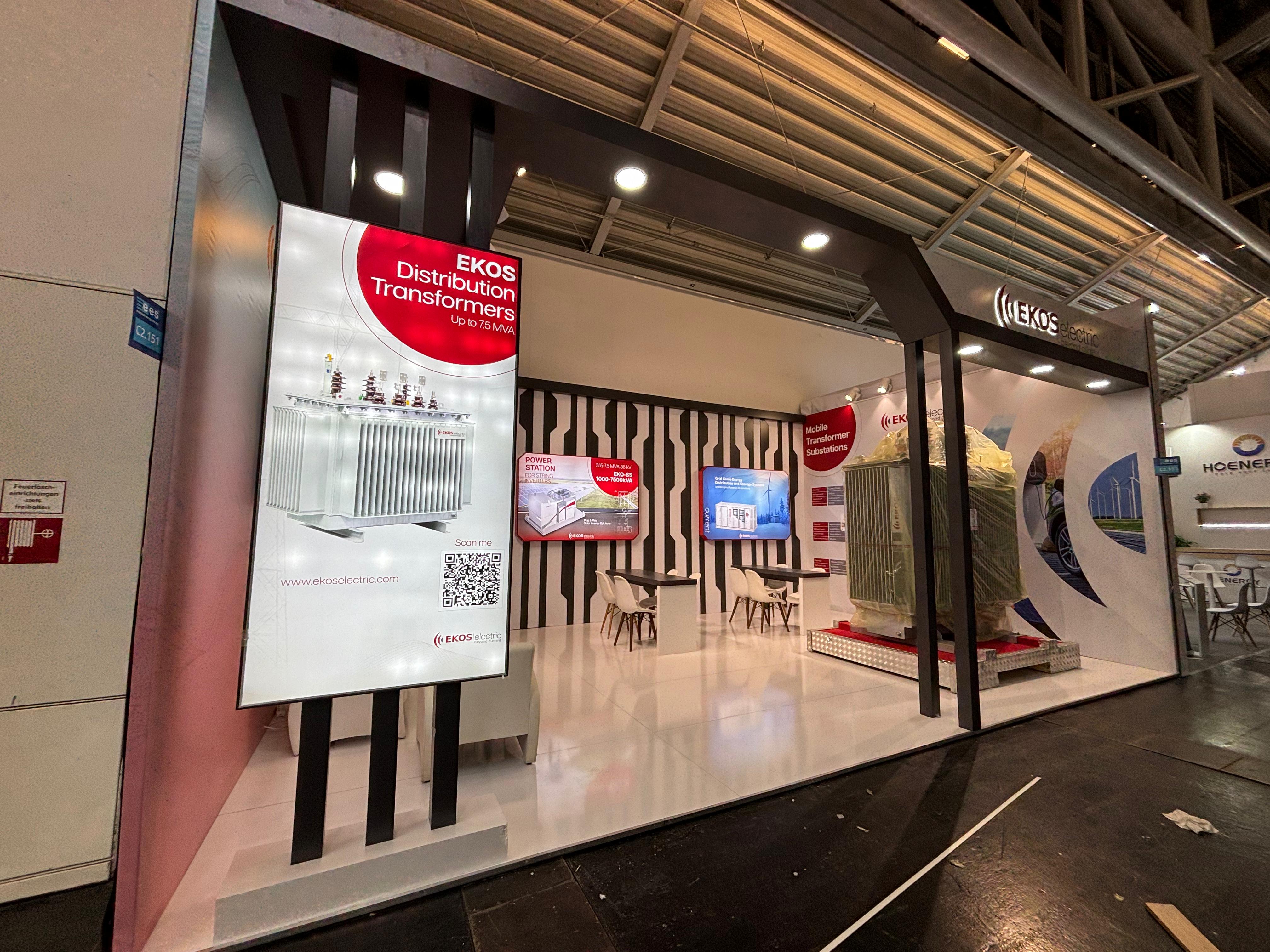 Ekos Electric exhibition stand at Intersolar 2025 Munich, featuring a clean industrial design with black, white, and red branding and a large transformer display.