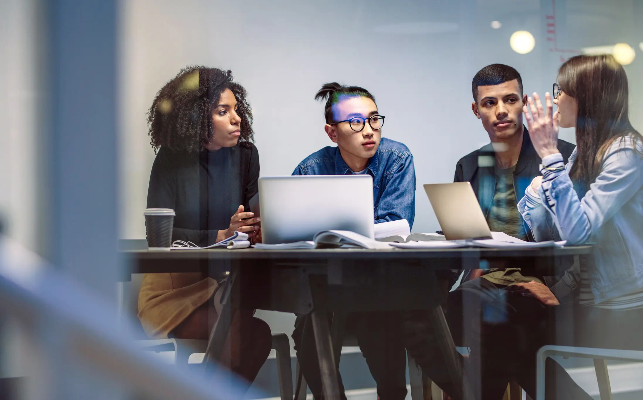 Four diverse young professionals collaborating around laptops in a modern meeting room