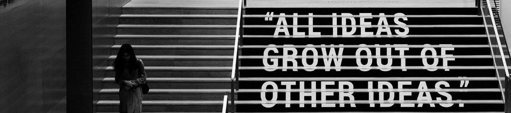 Black and white staircase with quote "All ideas grow out of other ideas," person standing beside stairs.