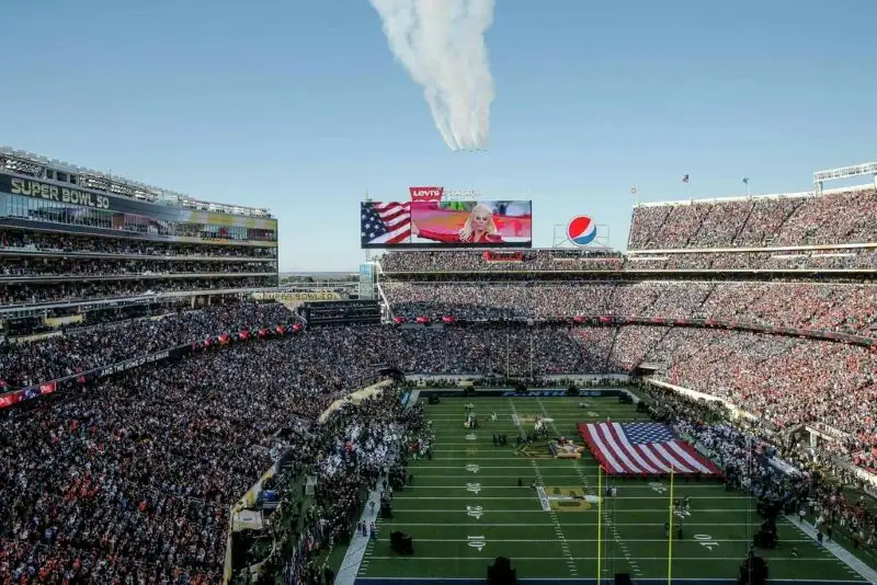 A talent recruiter with a soft smile working on her laptop in the office. The angle is on her face so we can't see what's is on the screen. She is wearing a blazer 