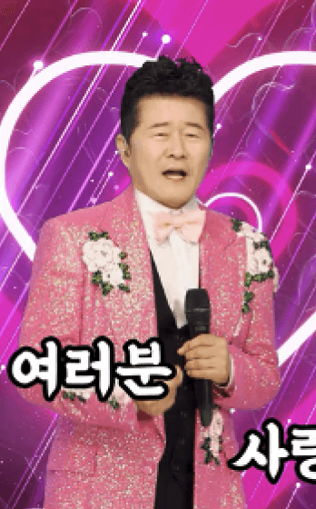 A realistic AI human singer wearing a glittery pink suit performs on stage with a glowing heart background. Karaoke-style text saying “I love you everyone” appears on screen.