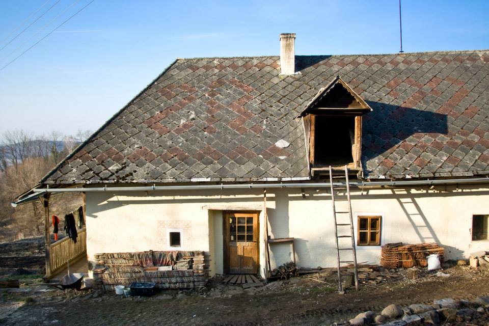 A smiling young man with crossed arms, wearing a plaid shirt and white t-shirt, poses against a dark background.