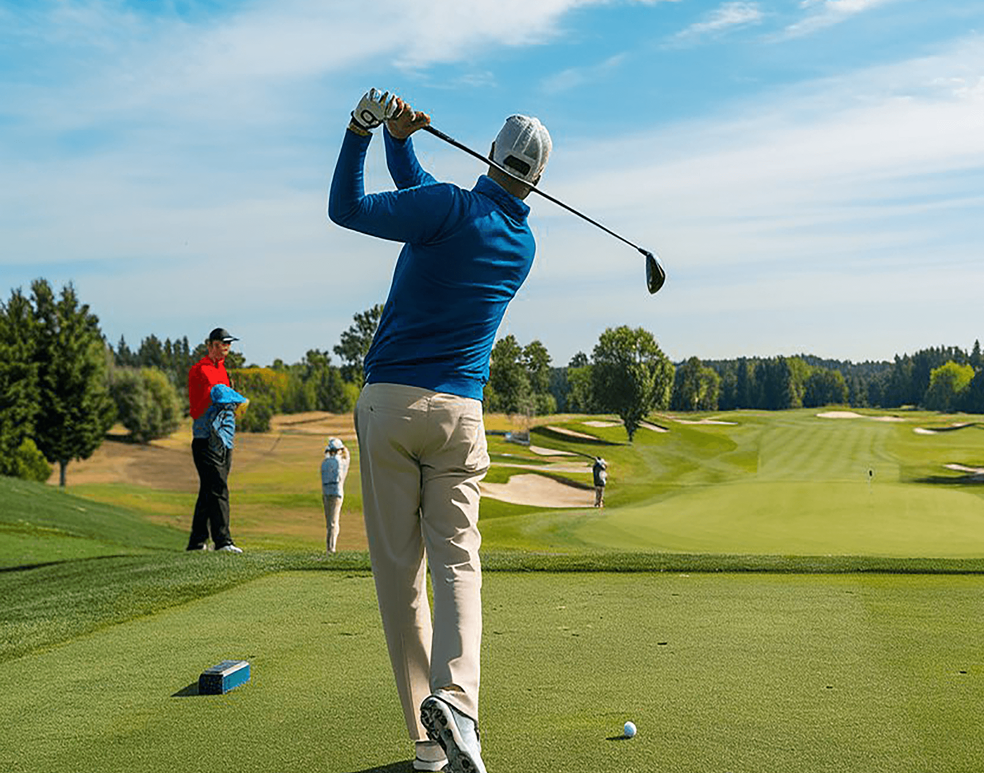 A man in a blue shirt and white shorts is playing golf, while three women in dresses