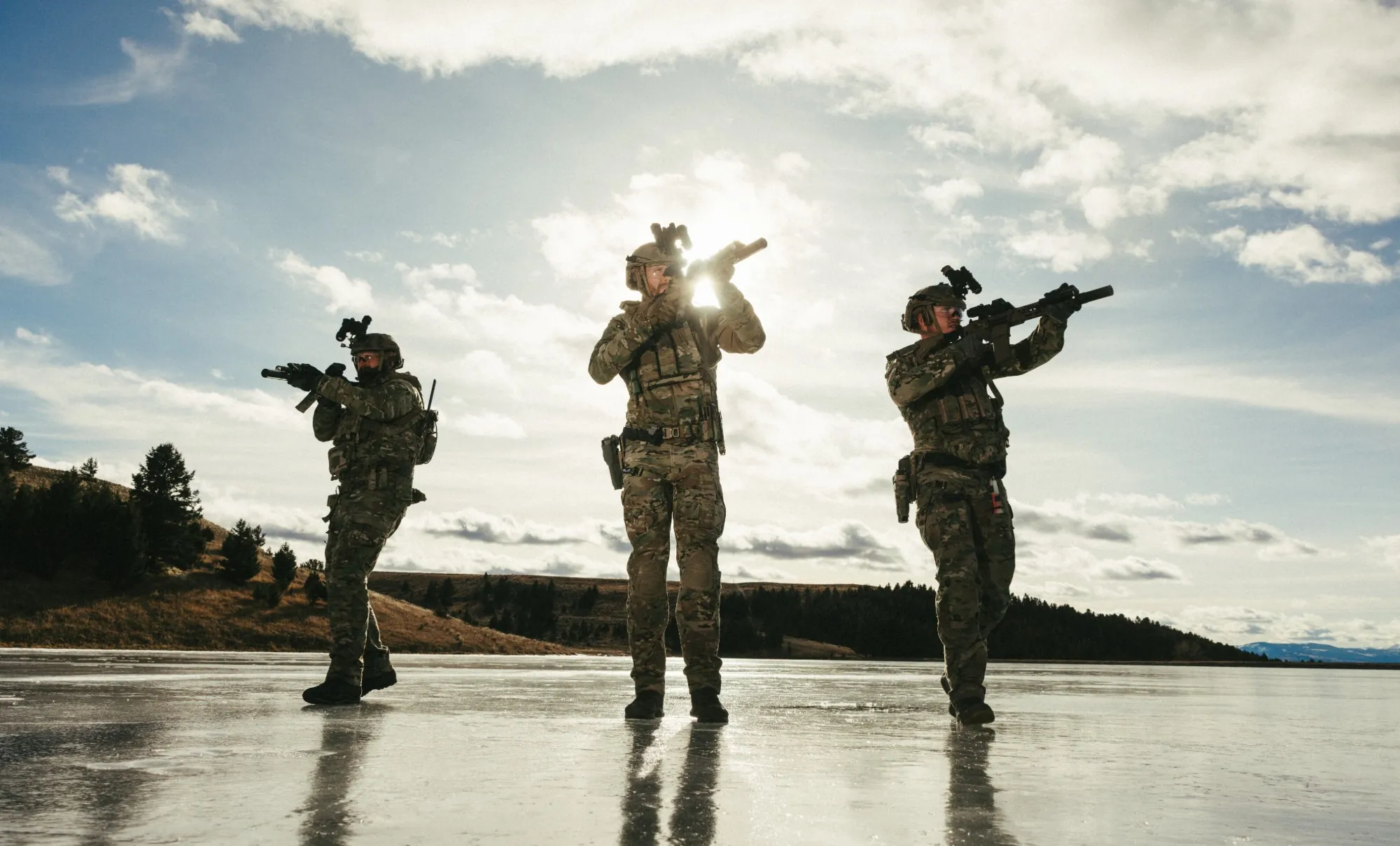 Three soldiers in multicam advancing across a frozen lake under a bright sky