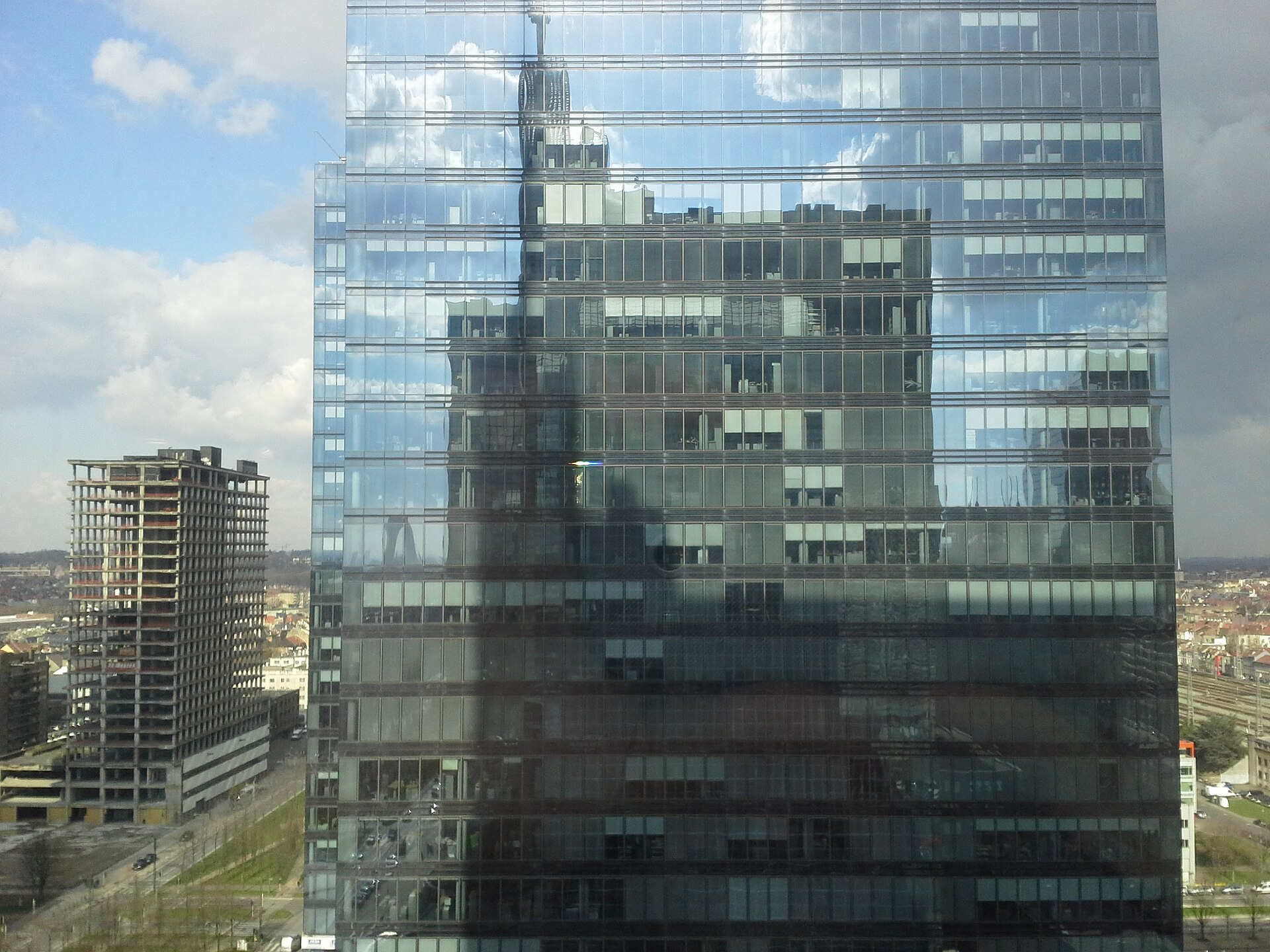 Een glazen kantoortoren in de Brusselse Noordwijk, met de omliggende skyline weerspiegeld in de gevel.
