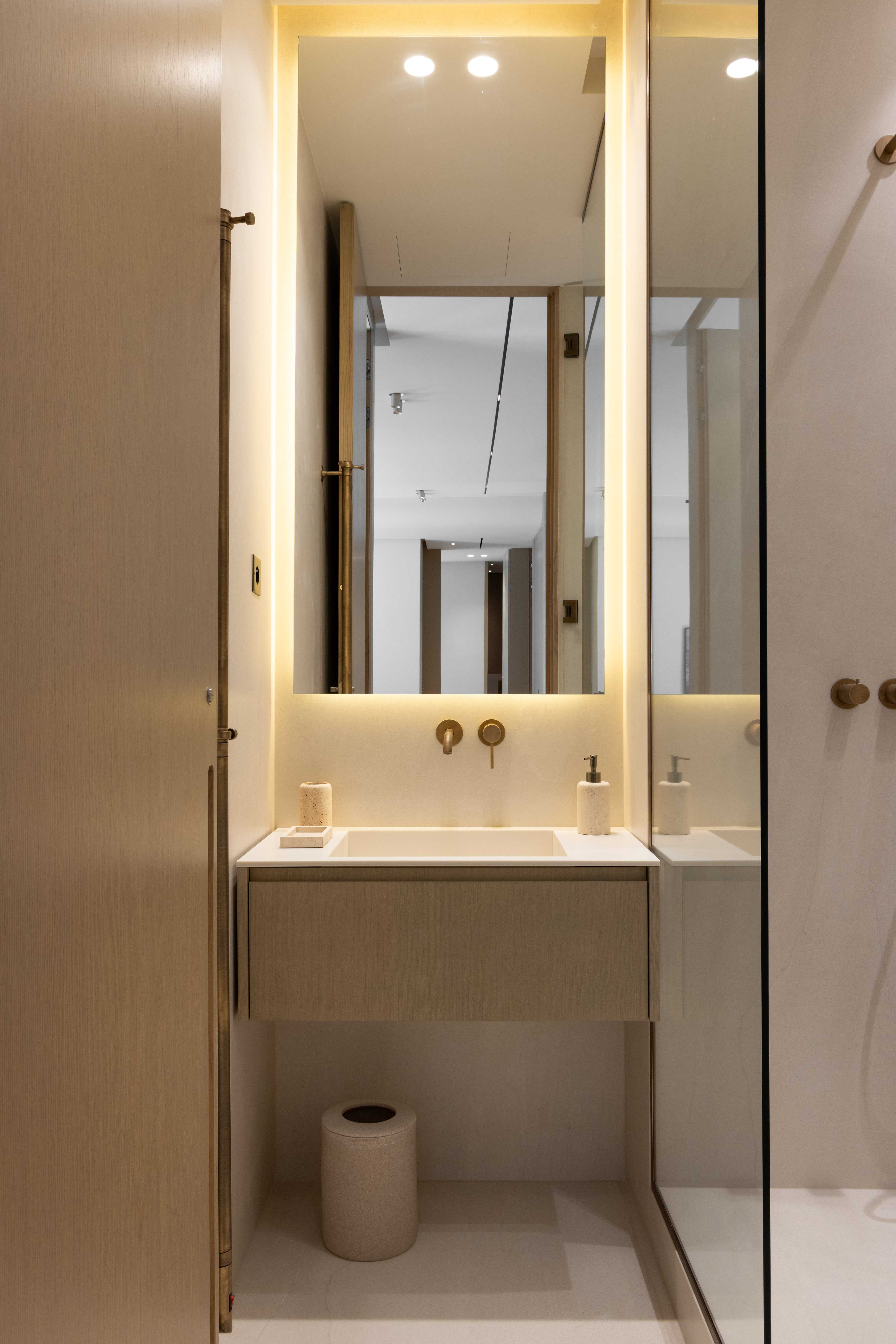 Salle d'eau avec vasque suspendue, miroir retroeclaire, robinetterie doree et paroi de douche vitree