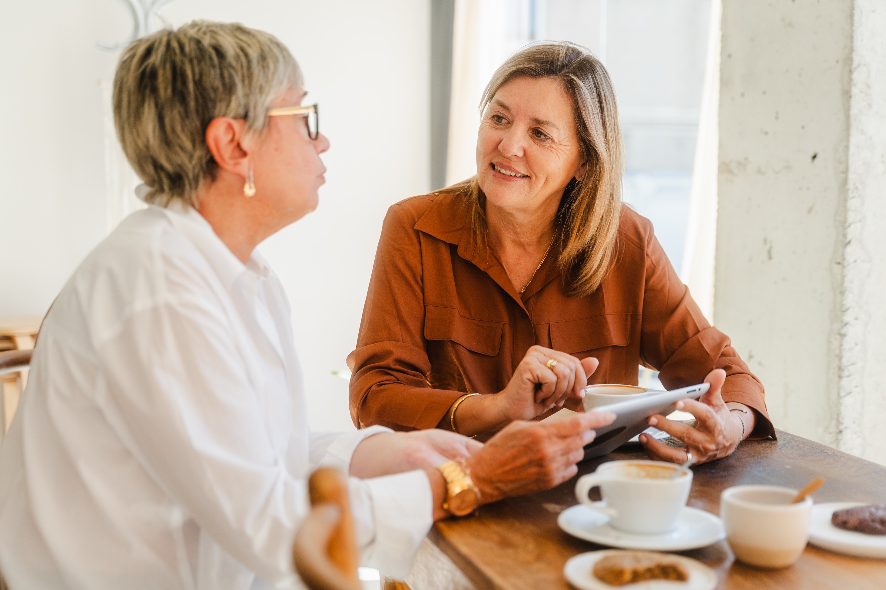 A financial advisor and a retirement saver discuss information on a tablet displaying the Pontera platform at a wooden table with coffee cups and snacks