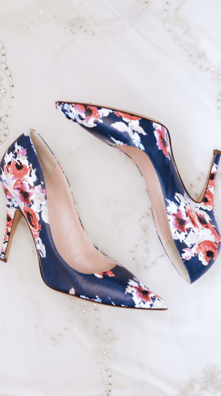 Women’s Pumps with four-inch heels and floral print on navy blue background laying on a marble surface
