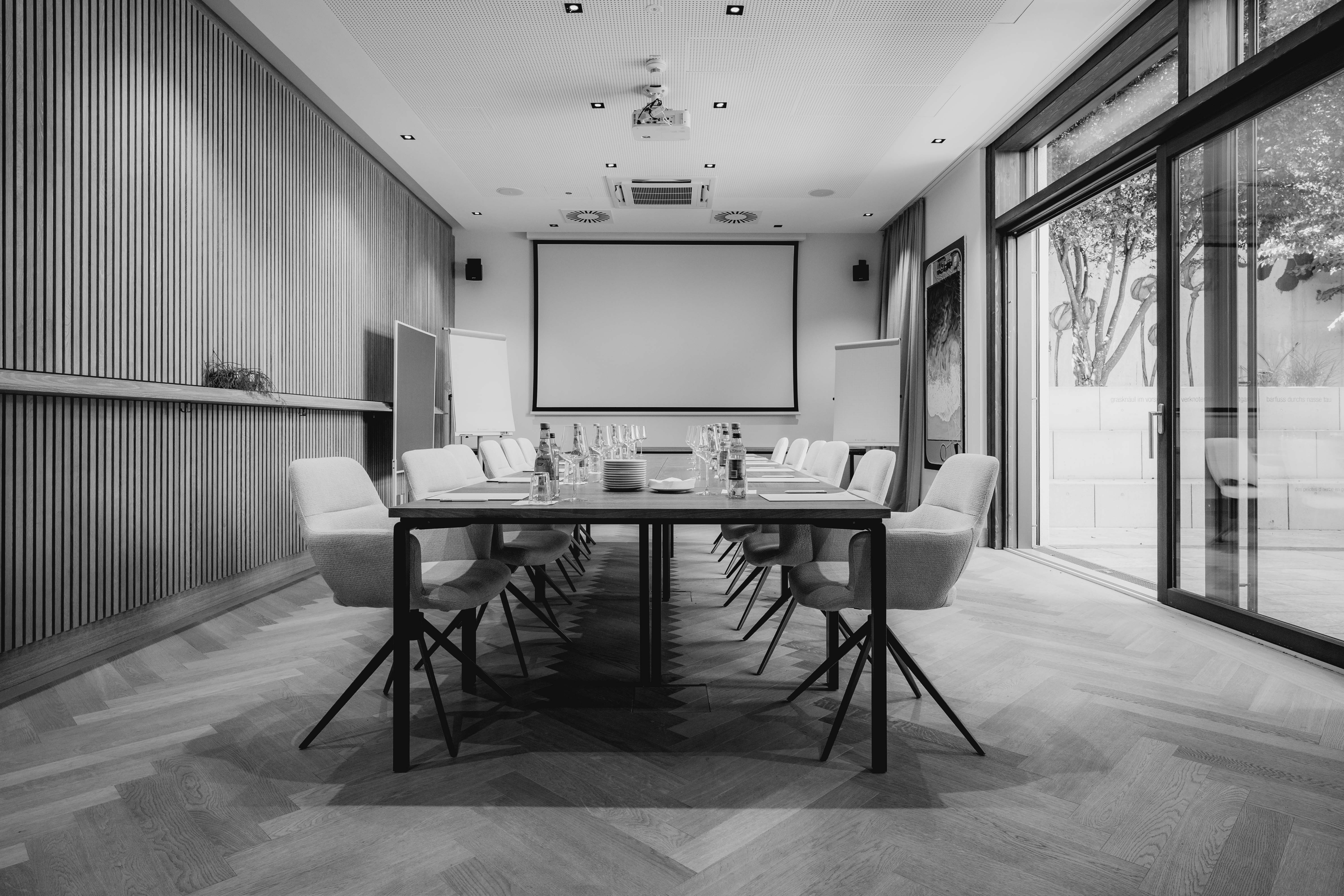 A modern classroom in black and white, featuring desks, a large screen, and windows with natural light.