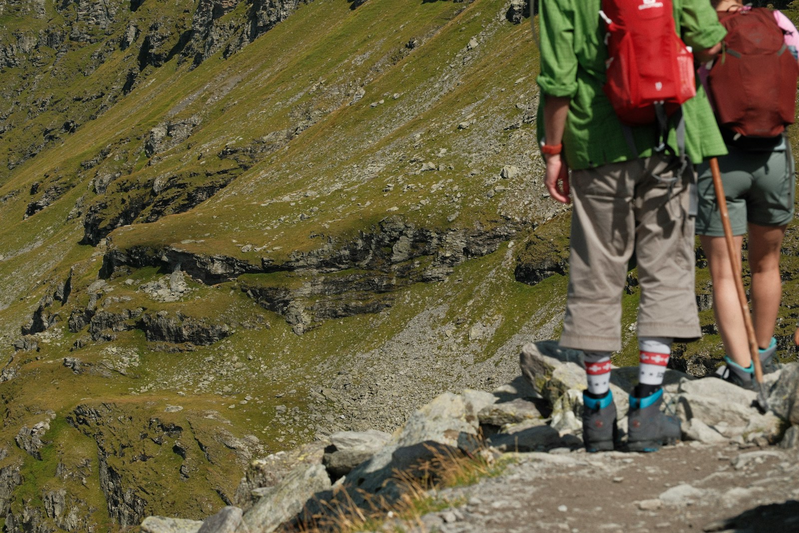 Hikers on a rocky trail above a steep green slope