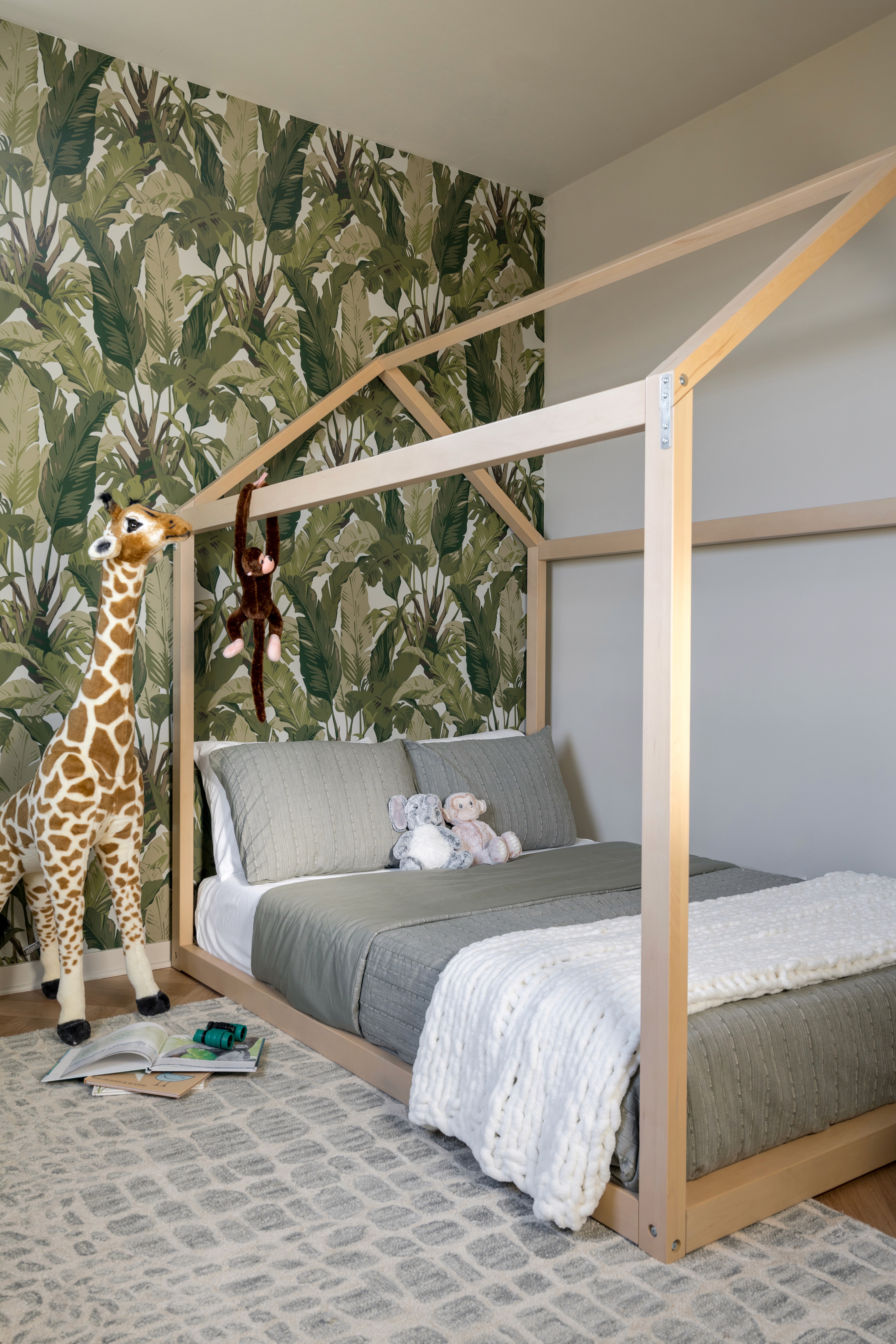 Jungle themed boy's bedroom with wood framed floor bed, green jungle print wall paper, and jungle animal decor