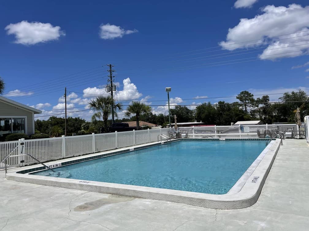 Image of sunny oasis style inground pool with white fence surrounding the pool deck