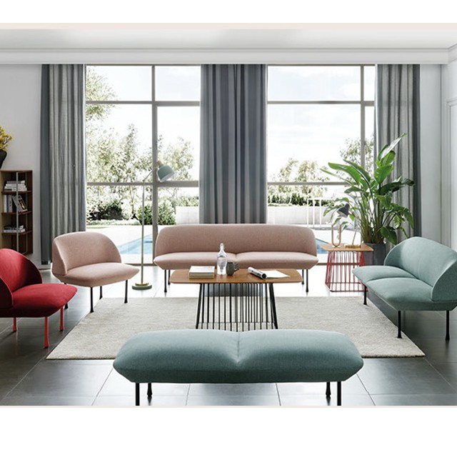 Modern luxury living room furniture set featuring a curved pink sofa, teal upholstered loveseat, and colorful accent chairs. The minimalist interior design includes a designer coffee table with a wire frame base and large windows, perfect for upscale home styling inspiration.