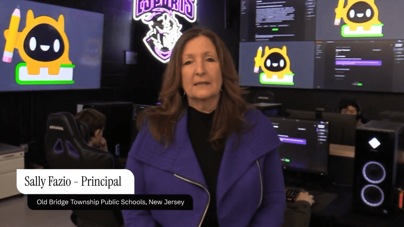 A man wearing a black polo shirt and a light-colored baseball cap sits in a high-backed chair, facing the camera. He is wearing over-ear headphones with an attached microphone, suggesting he is speaking or participating in an online meeting or recording. The background includes a dark cabinet and a desk with computer equipment, indicating a home office or studio setting.