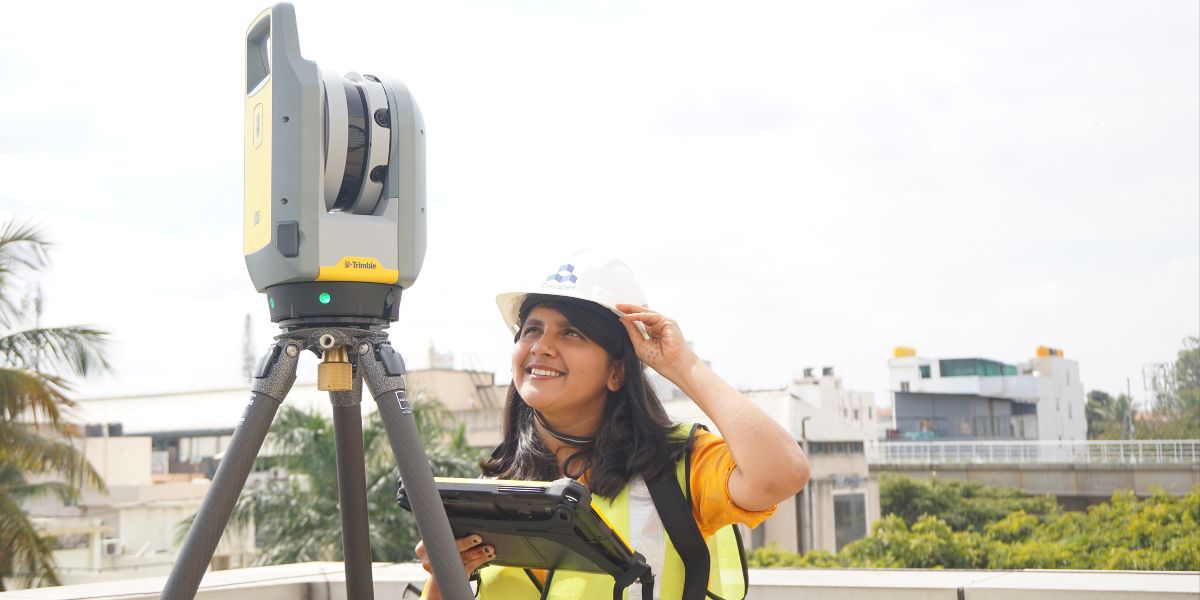 A man stands while two people sit at a table in an office setting, smiling and engaged in conversation. The mood is friendly and collaborative.