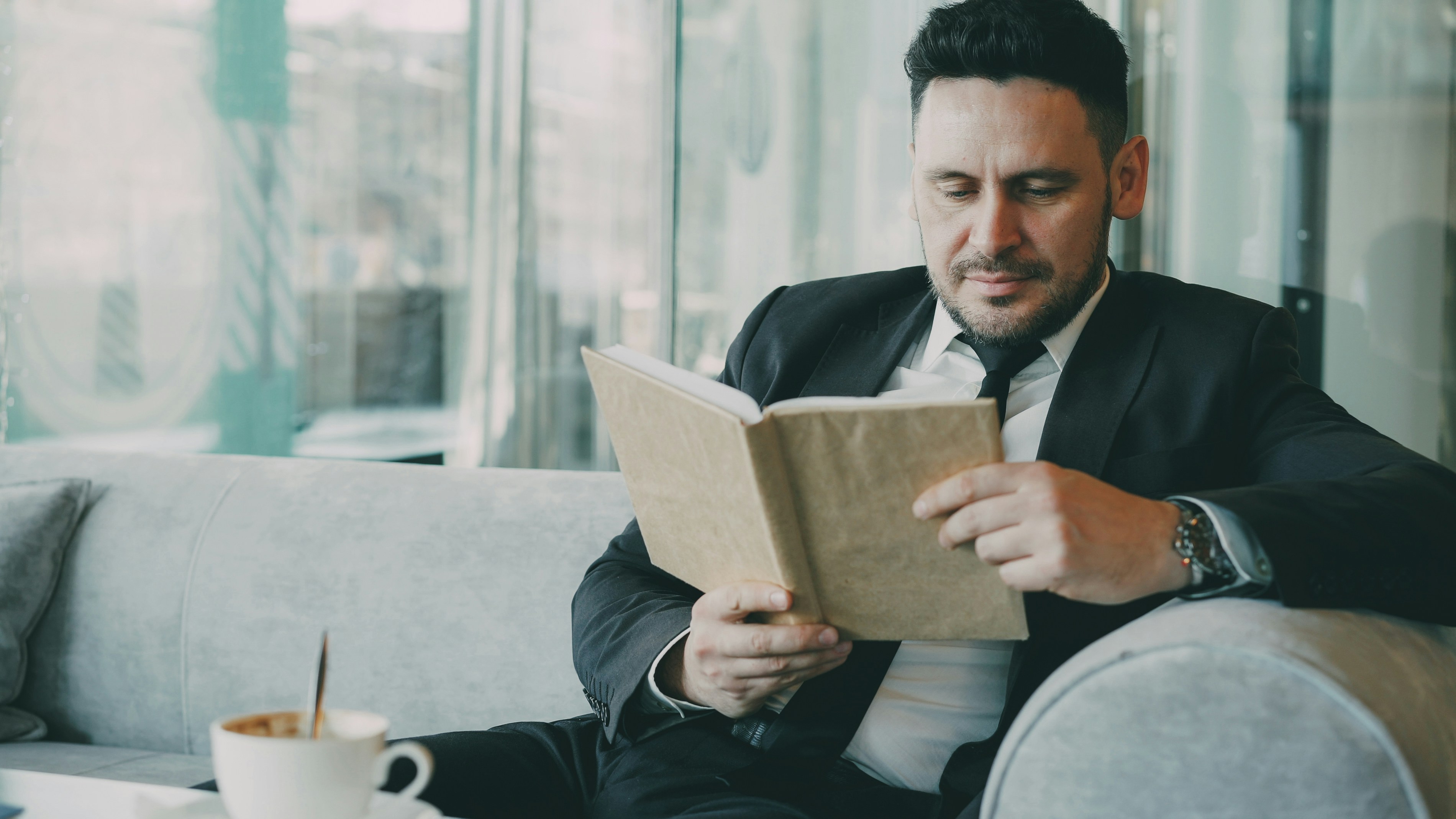 Man in suit reading a book on sofa