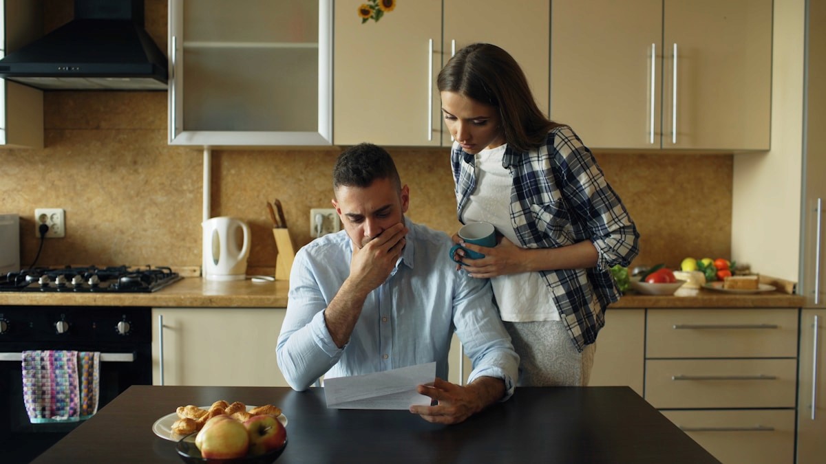 A worried couple reviewing paperwork at a kitchen table, suggesting frustration and hopelessness after trying everything