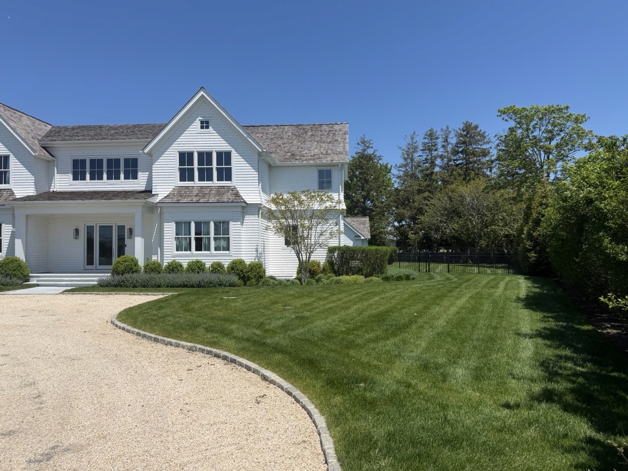 Striped green lawn in front of a white Hamptons-style estate home
