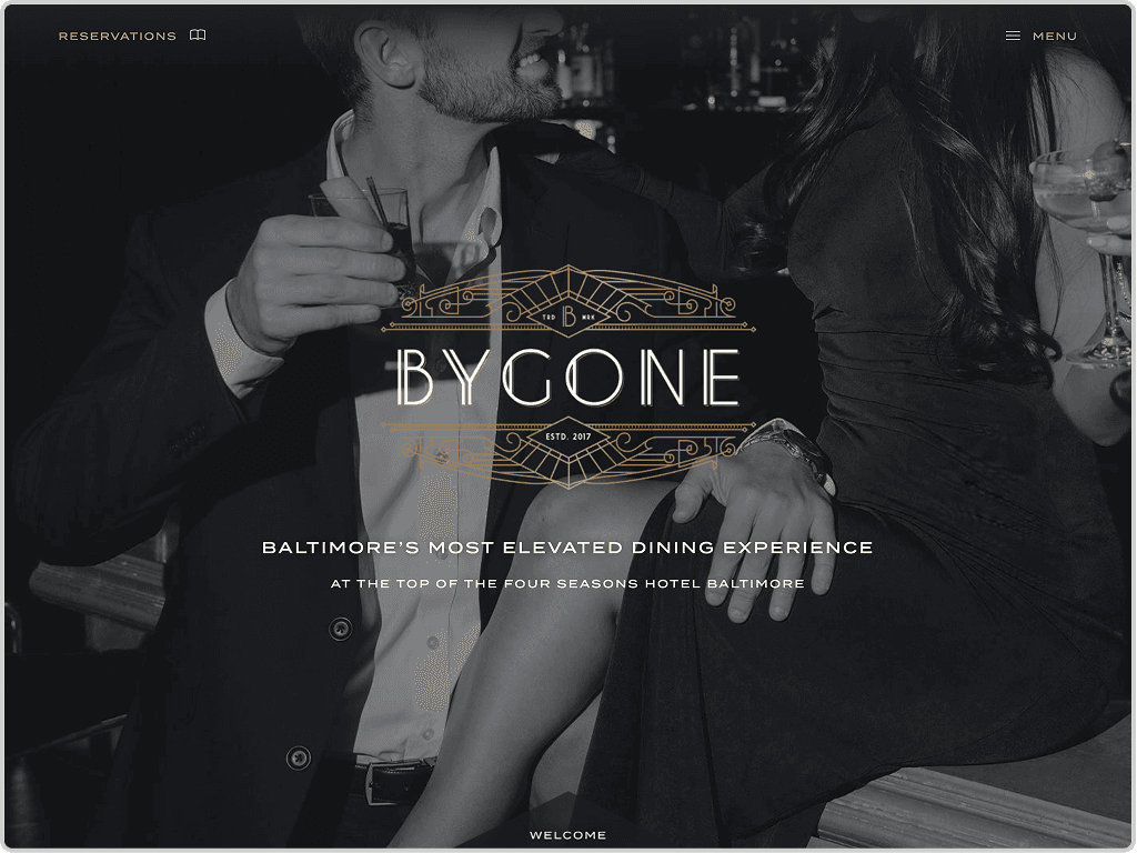 A man and woman dressed formally sit at a bar holding drinks, with the Bygone restaurant logo and text overlayed at the center of the image.