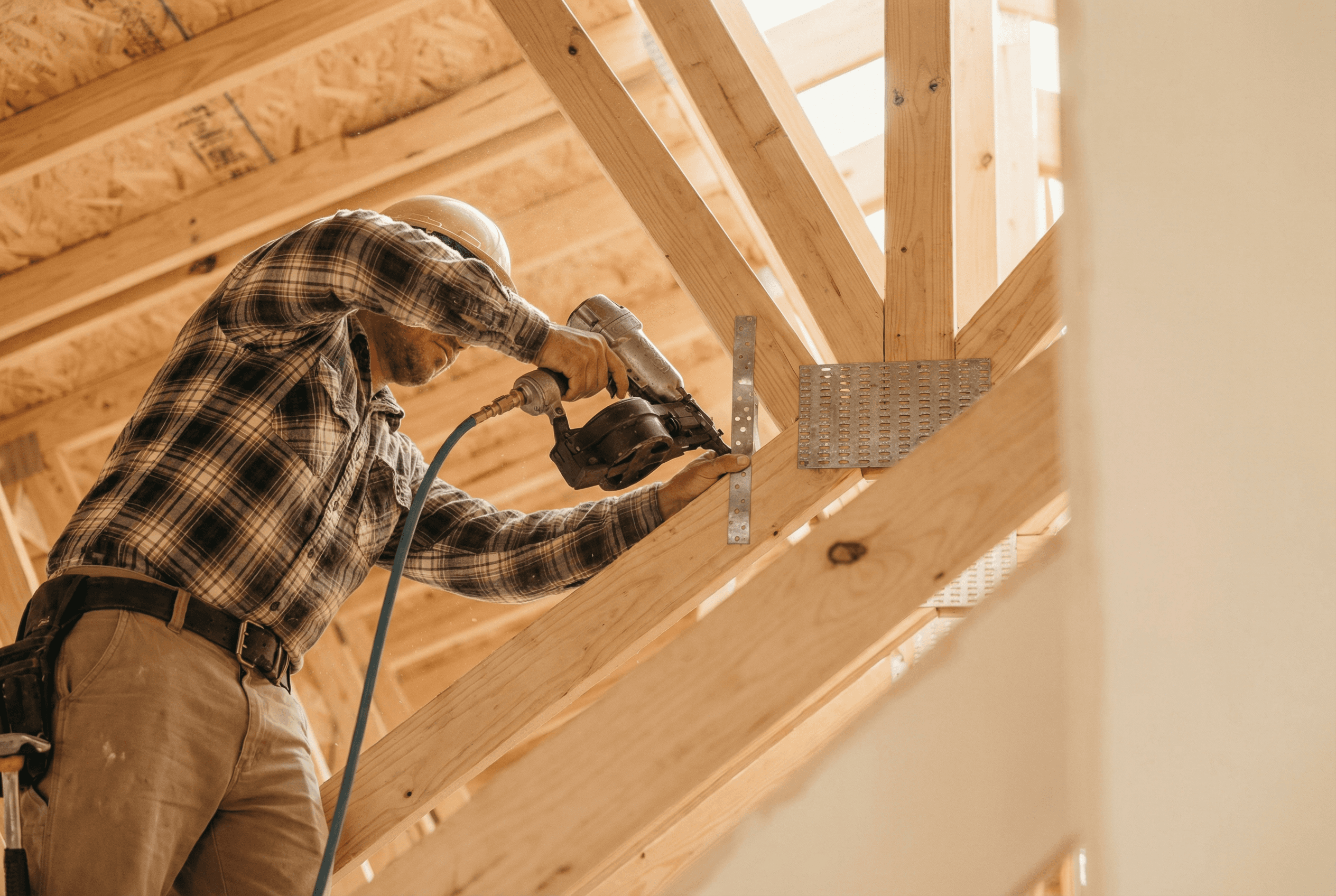 A professional contractor installing galvanized steel hurricane straps to wooden roof trusses, creating a continuous structural load path in a custom home.