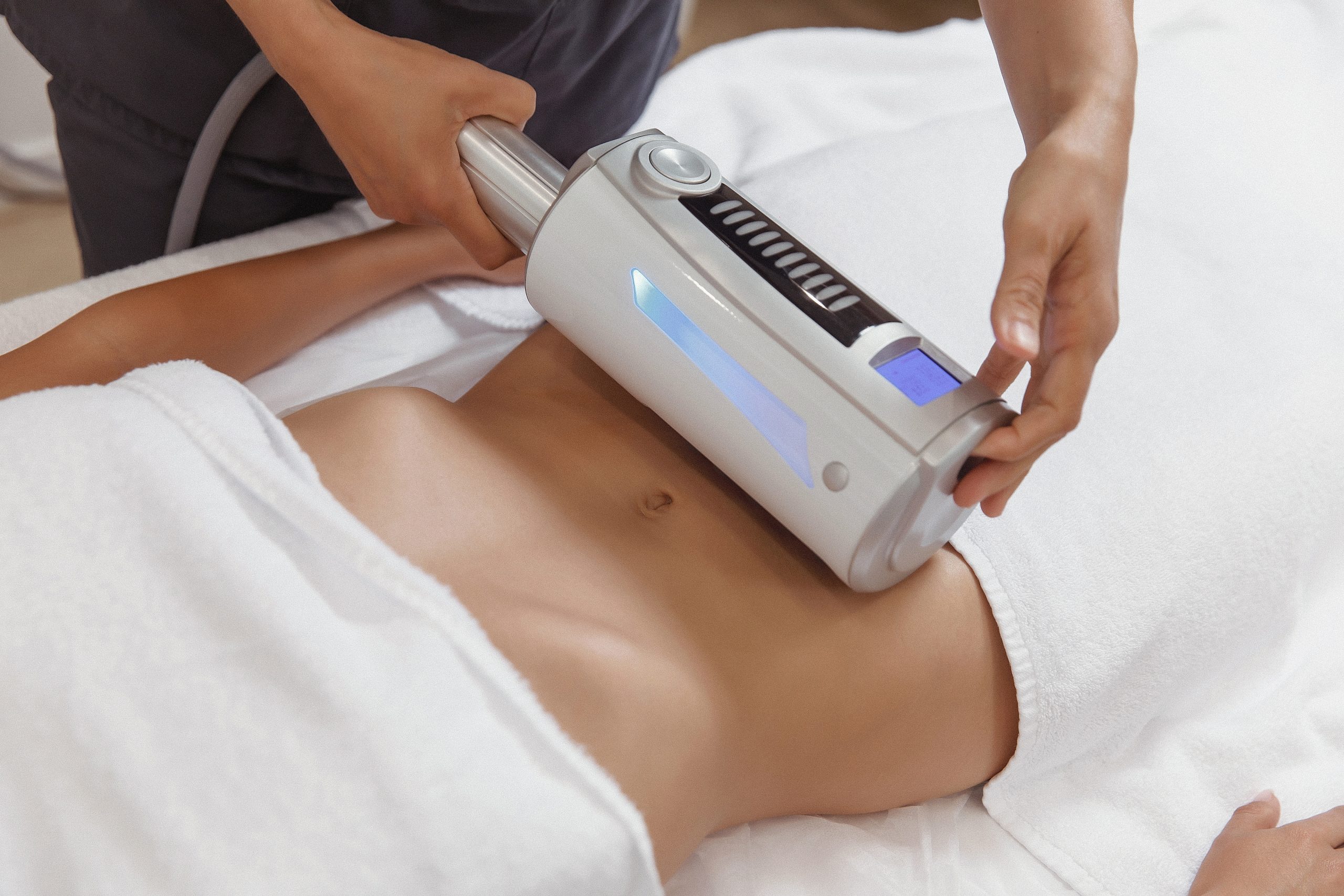 Professional performing a non-invasive body contouring treatment using advanced equipment on a client's abdomen, symbolizing cutting-edge aesthetic procedures.