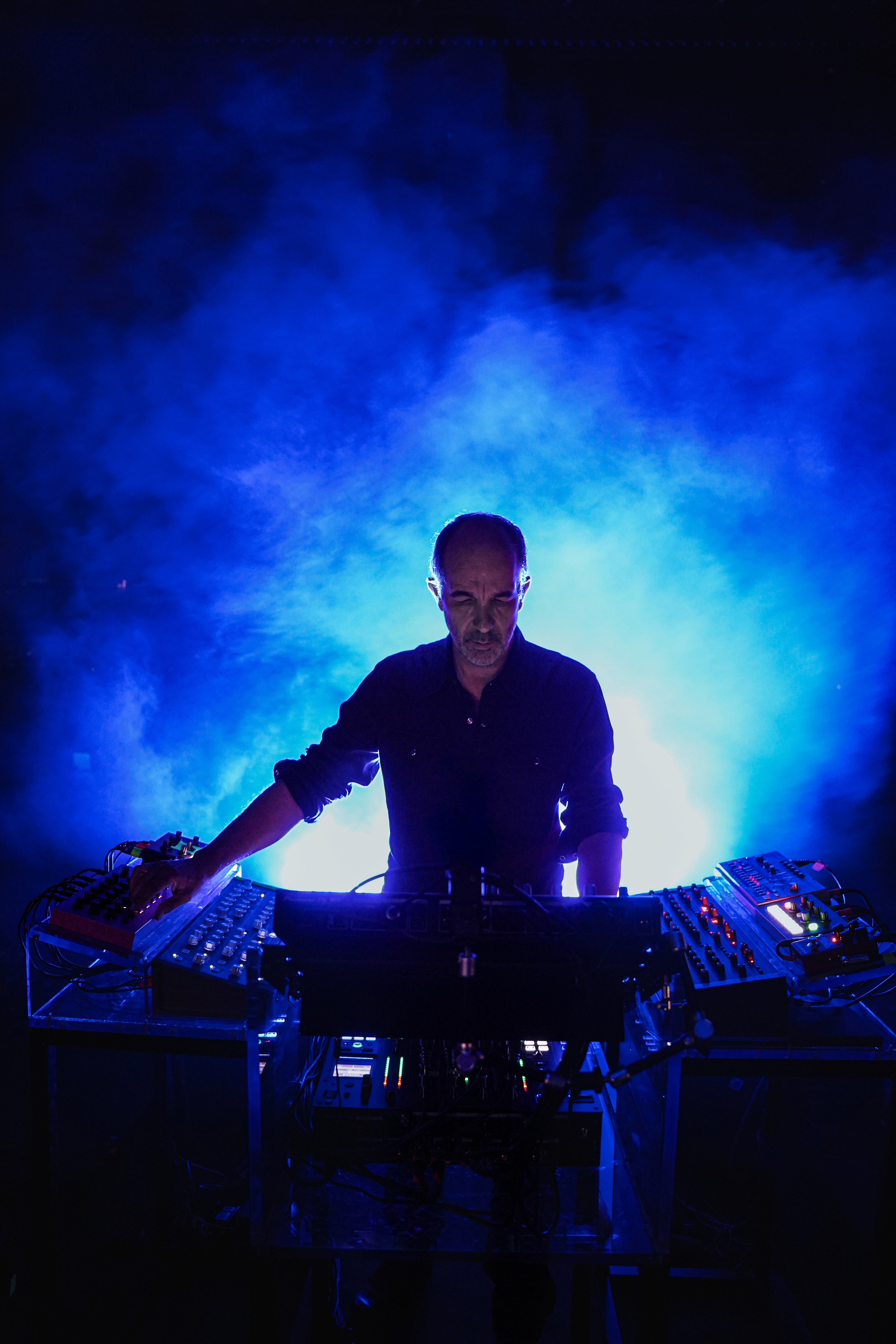 Etienne de Crecy derrière ses machines de mixage, entouré de fumée et de jeux de lumières de scène, capturé en plein live.