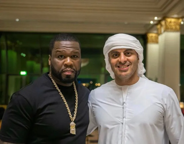 Black-and-white party photo of a smiling man in a check blazer among a crowd.
