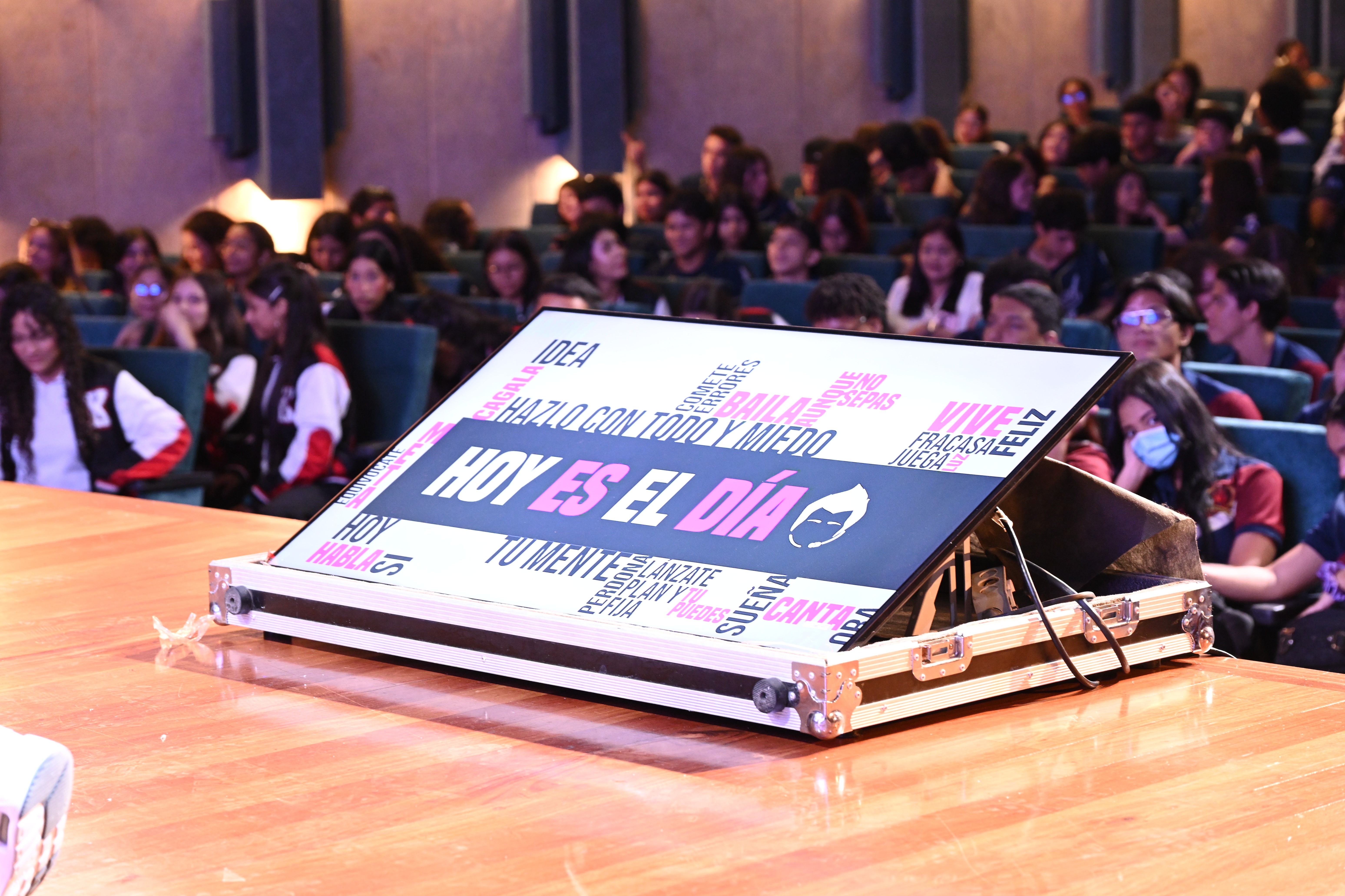 Escenario con un atril y un cartel que dice “Hoy es el día”, frente a un auditorio lleno de jovenes