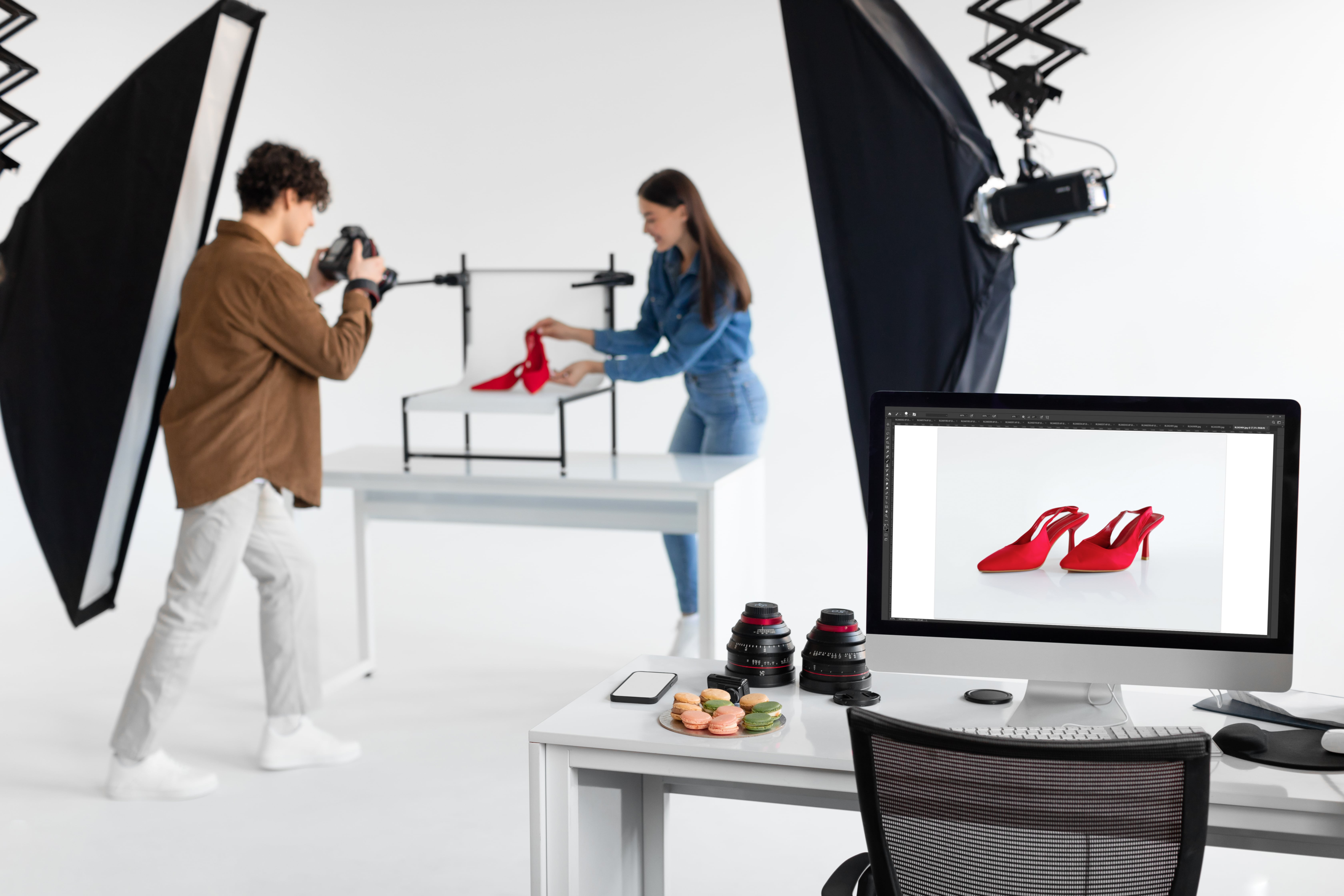 Professional product photography setup with a photographer shooting red high heels in a white studio with softbox lighting and computer post-processing.