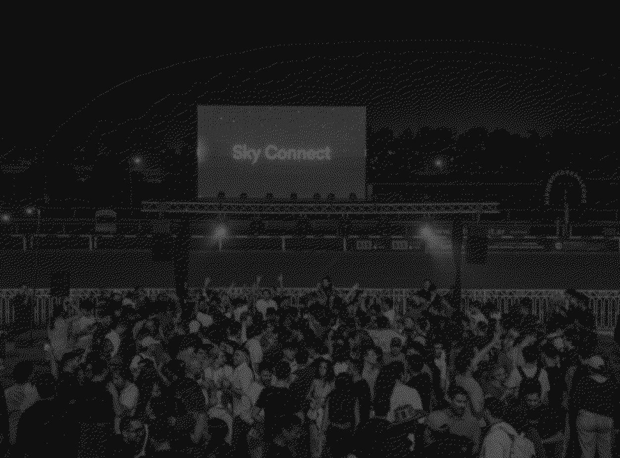 Three people in conversation with warm lighting, including a person wearing a hat and another person wrapped in what appears to be a textured shawl or sweater.