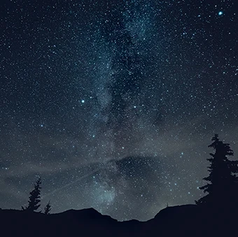 Rozgwieżdżone niebo z Drogą Mleczną nad ciemnym lasem i konturami gór, nocna fotografia z długim czasem naświetlania