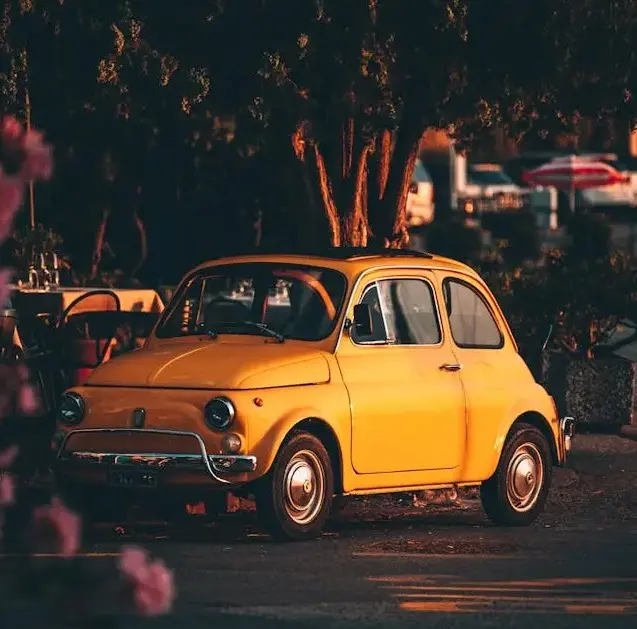 Vintage Fiat 500 in a European village square, symbol of slow mobility and authentic local living