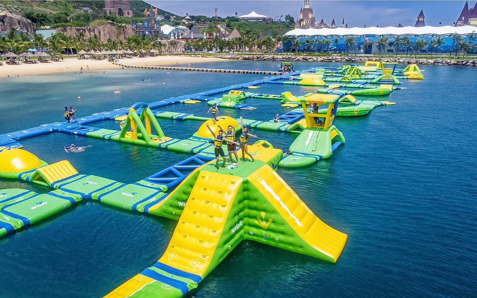 Floating water park with slides and obstacles at Splash Bay, featuring people enjoying activities.