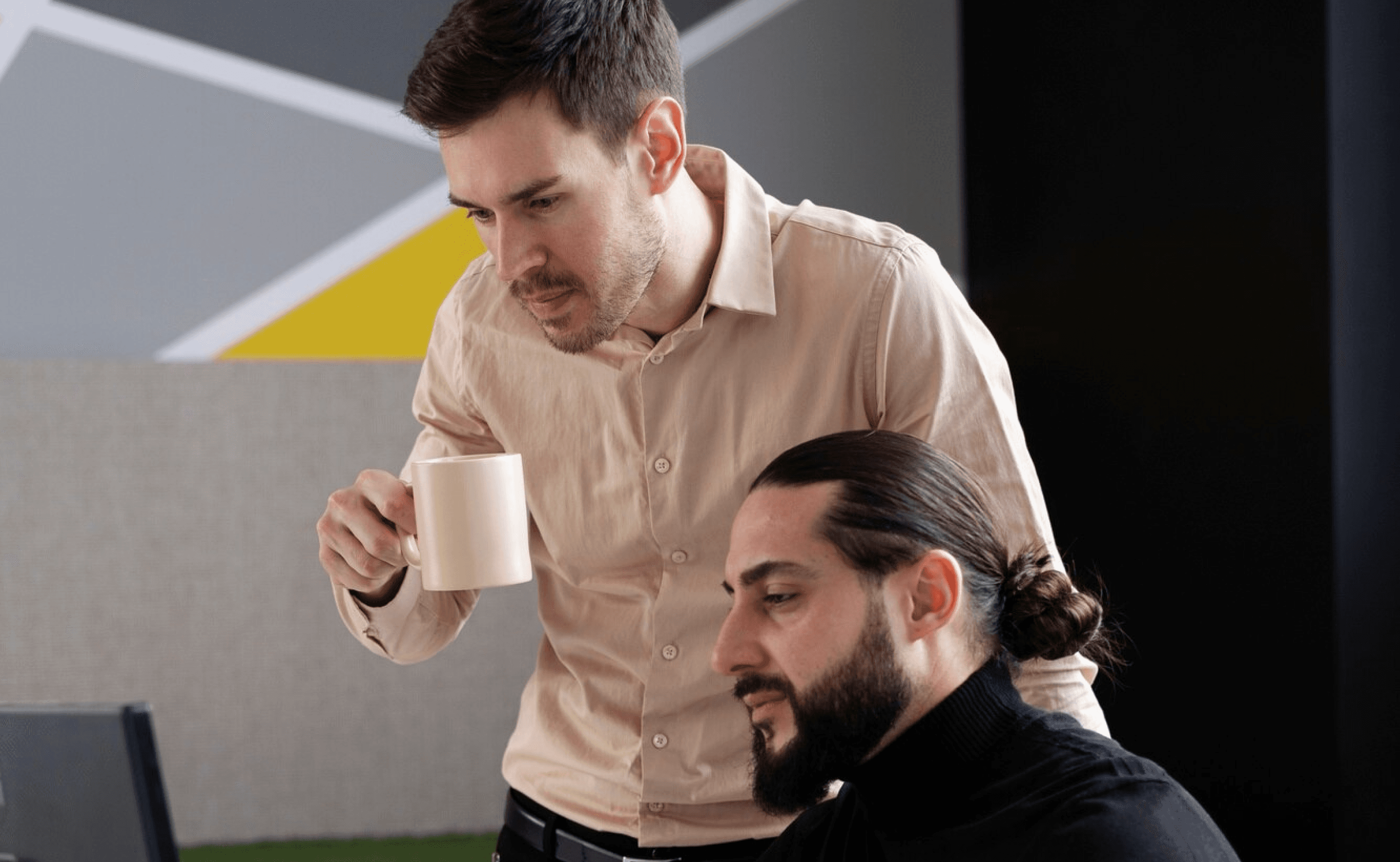 Two people collaborating at a desk, one pointing at a computer screen with a pen