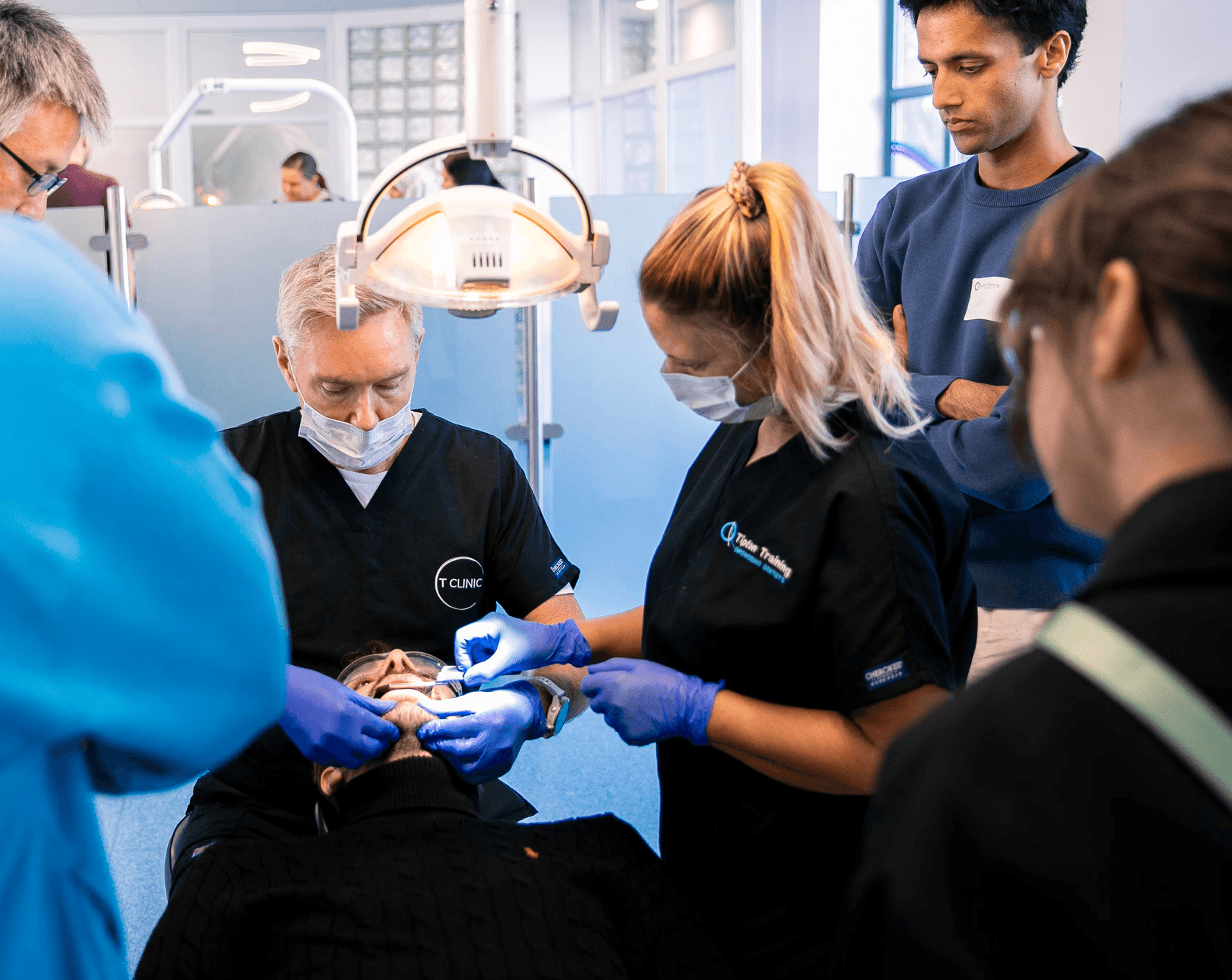 Portrait of a young man in a brown coat and beige turtleneck, with light brown hair and a calm expression against a gray background.