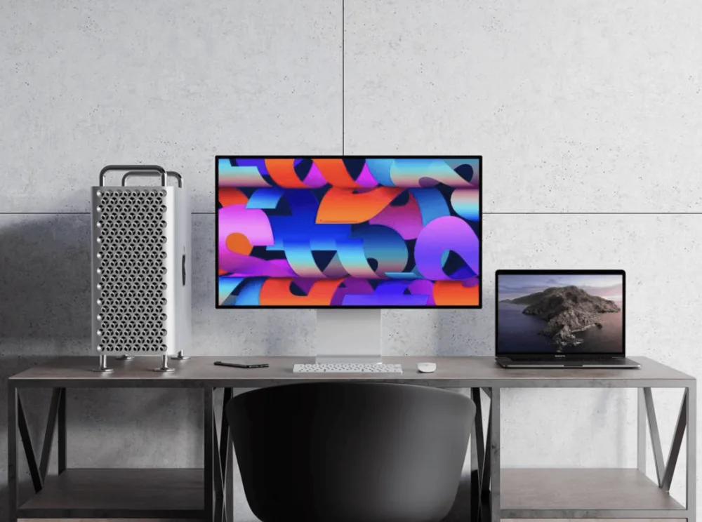 A modern workspace featuring a desktop computer with a vibrant, abstract display, a Mac Pro tower, and a MacBook displaying a scenic wallpaper. The setup rests on a sleek metal desk against a concrete wall.
