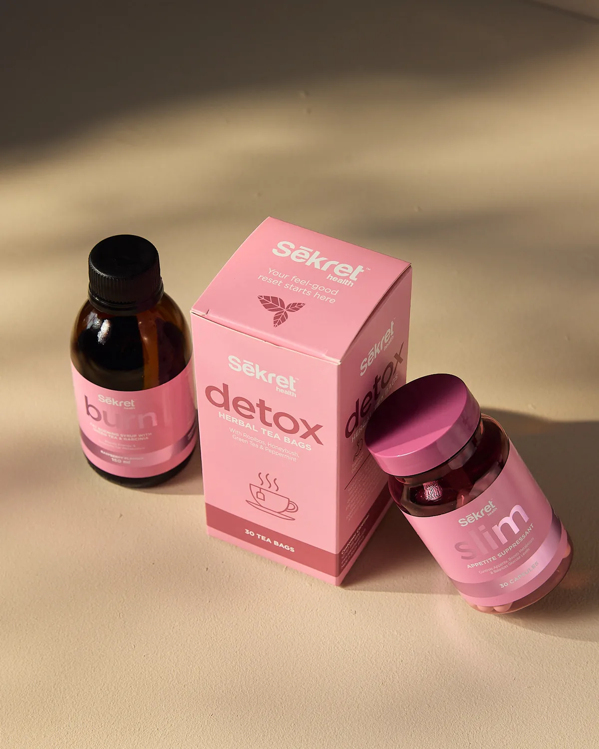 The Sēkret Detox tea box between a bottle of Burn syrup and Slim capsules