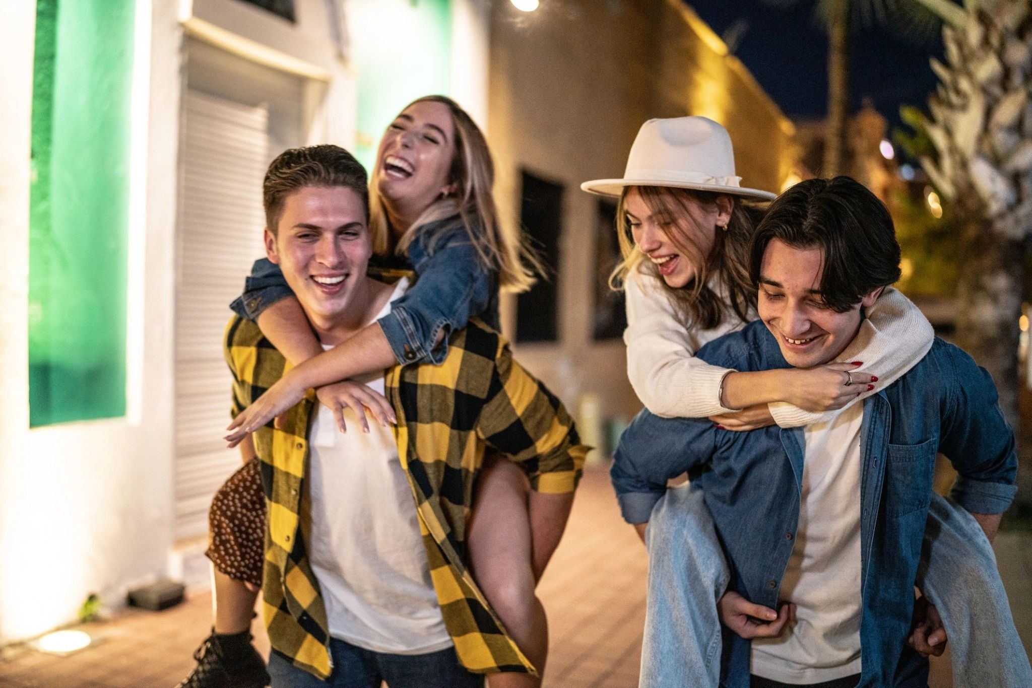 Two couples enjoying piggyback rides together during a night out.