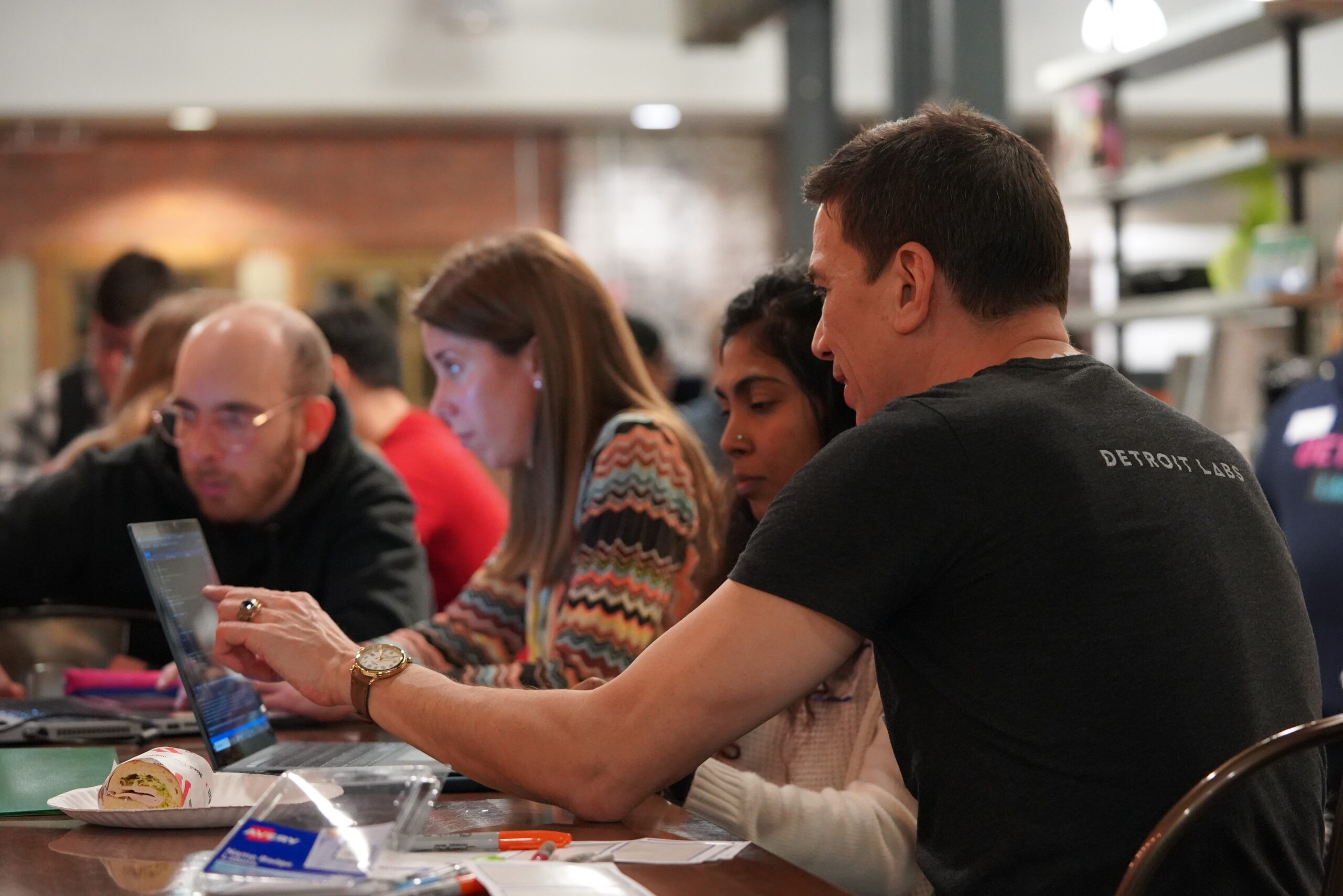 Detroit Labs team members gathered around a laptop at a long wooden table