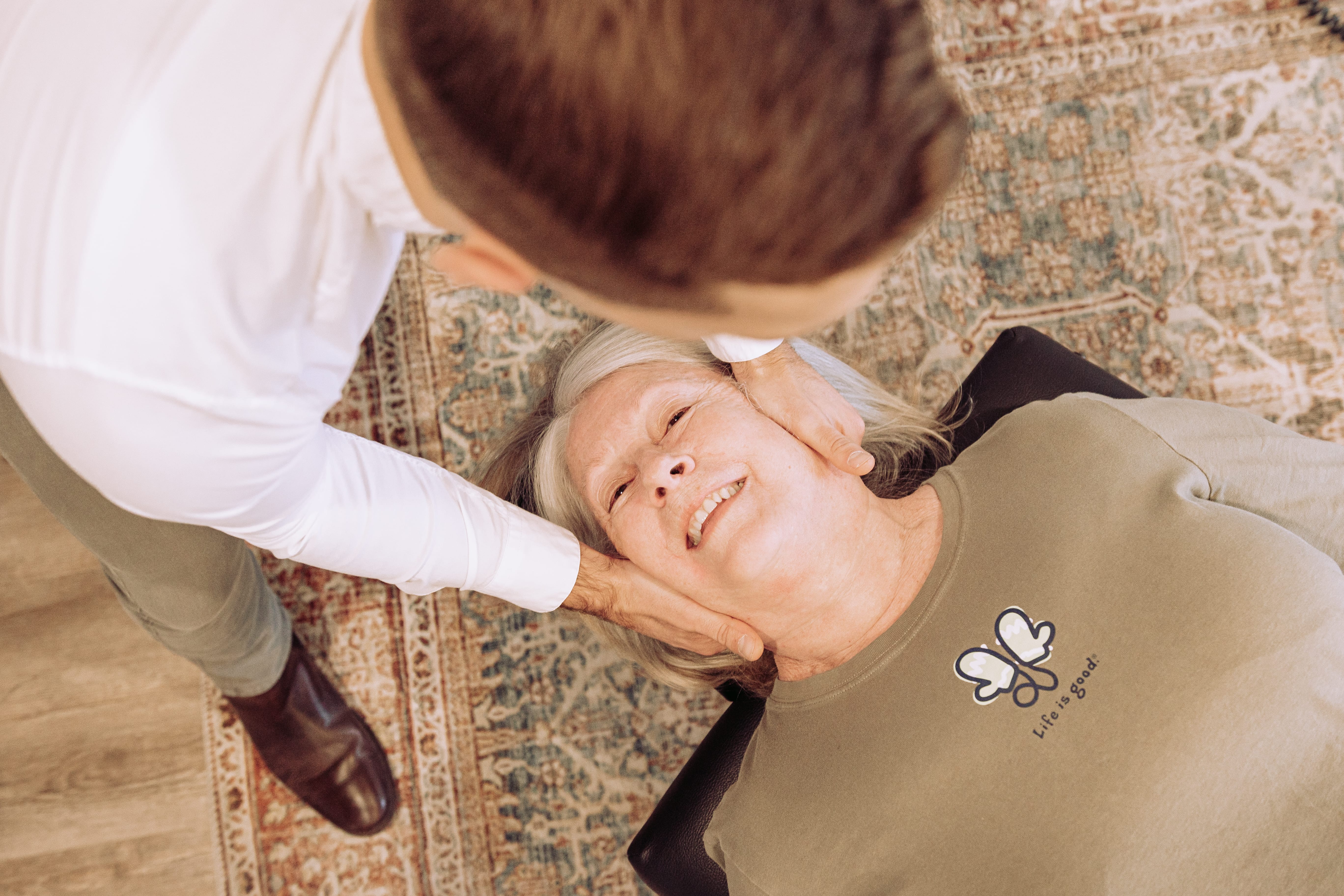 An overhead shot of a smiling woman getting her neck adjusted by a doctor.