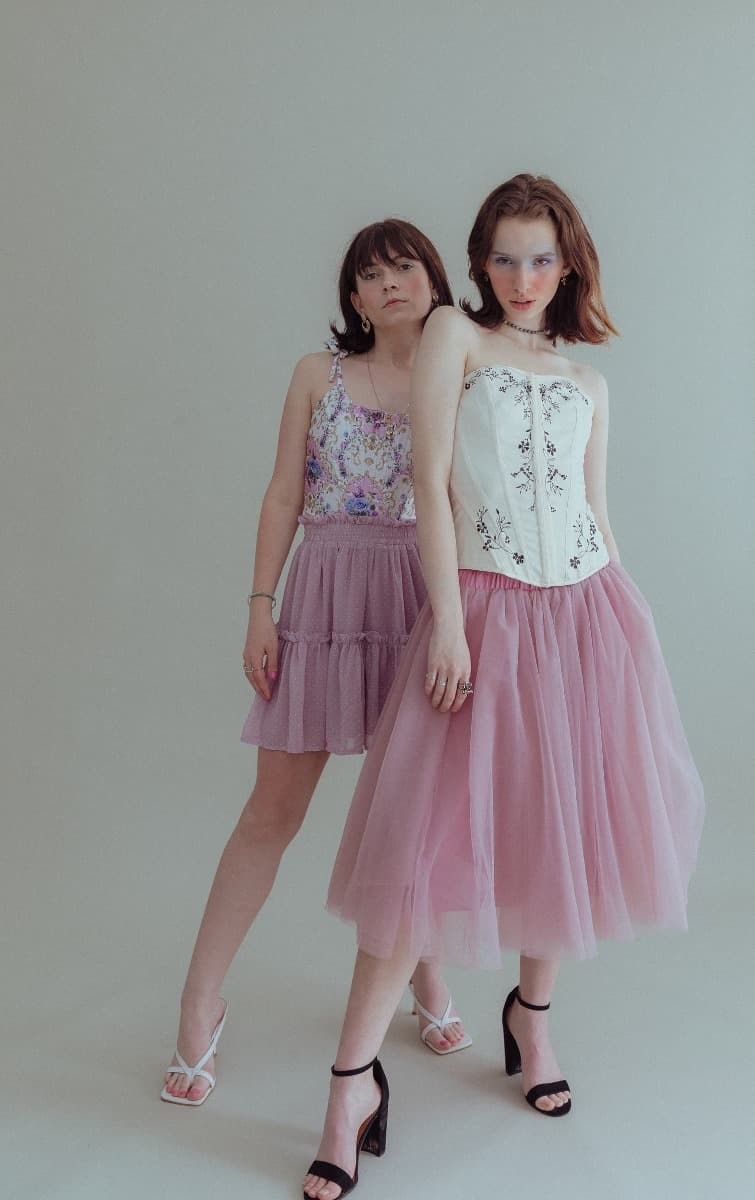 Models posing confidently in corset tops and pink skirts, showcasing an ethereal style at Revelator Studio, a Shreveport natural light studio.