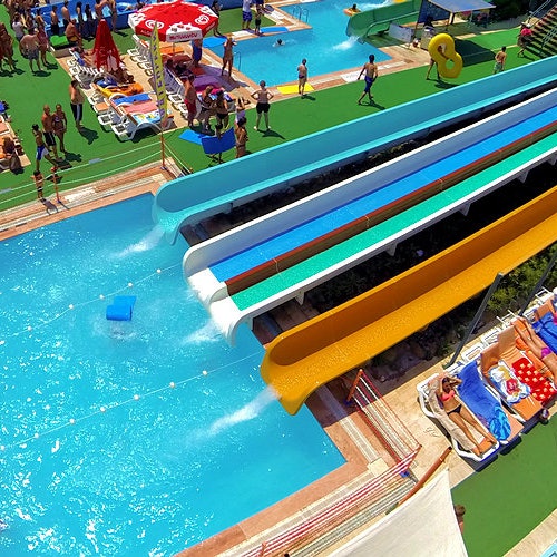 Flygvy över en vattenpark med flera vattenrutschbanor, pooler och människor som slappar eller simmar.