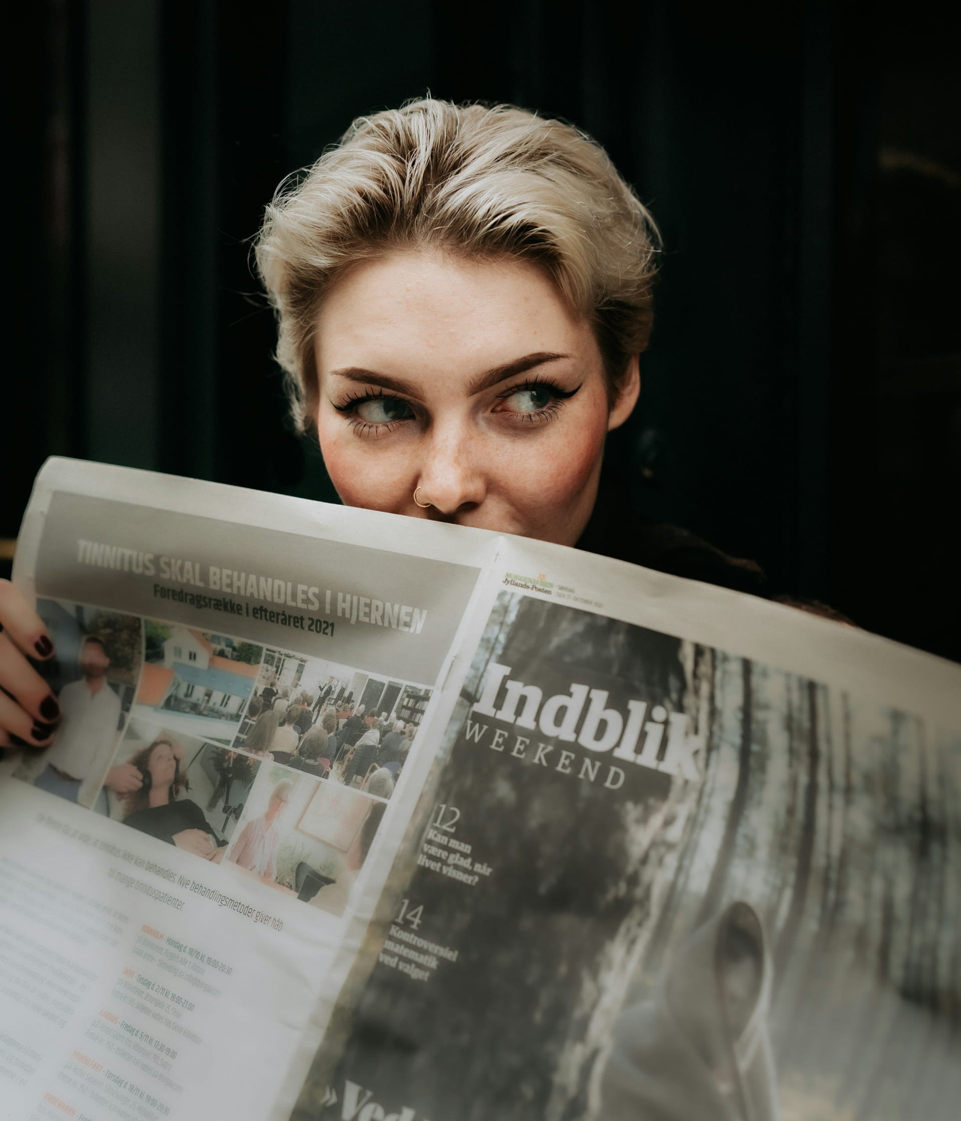 A mysteriously smiling woman covers her face with a newspaper