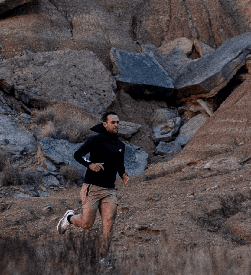 Man wearing olive green and orange sneakers with tall socks, standing on an urban street with a modern fence and skyscraper in the distance.