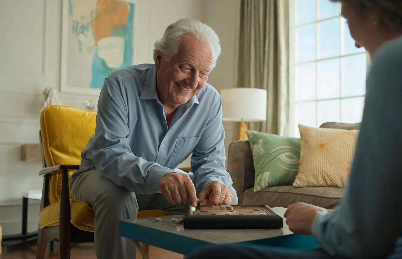 Older man playing a tabletop game with his caregiver during an at-home Parkinson's care visit, staying mentally engaged