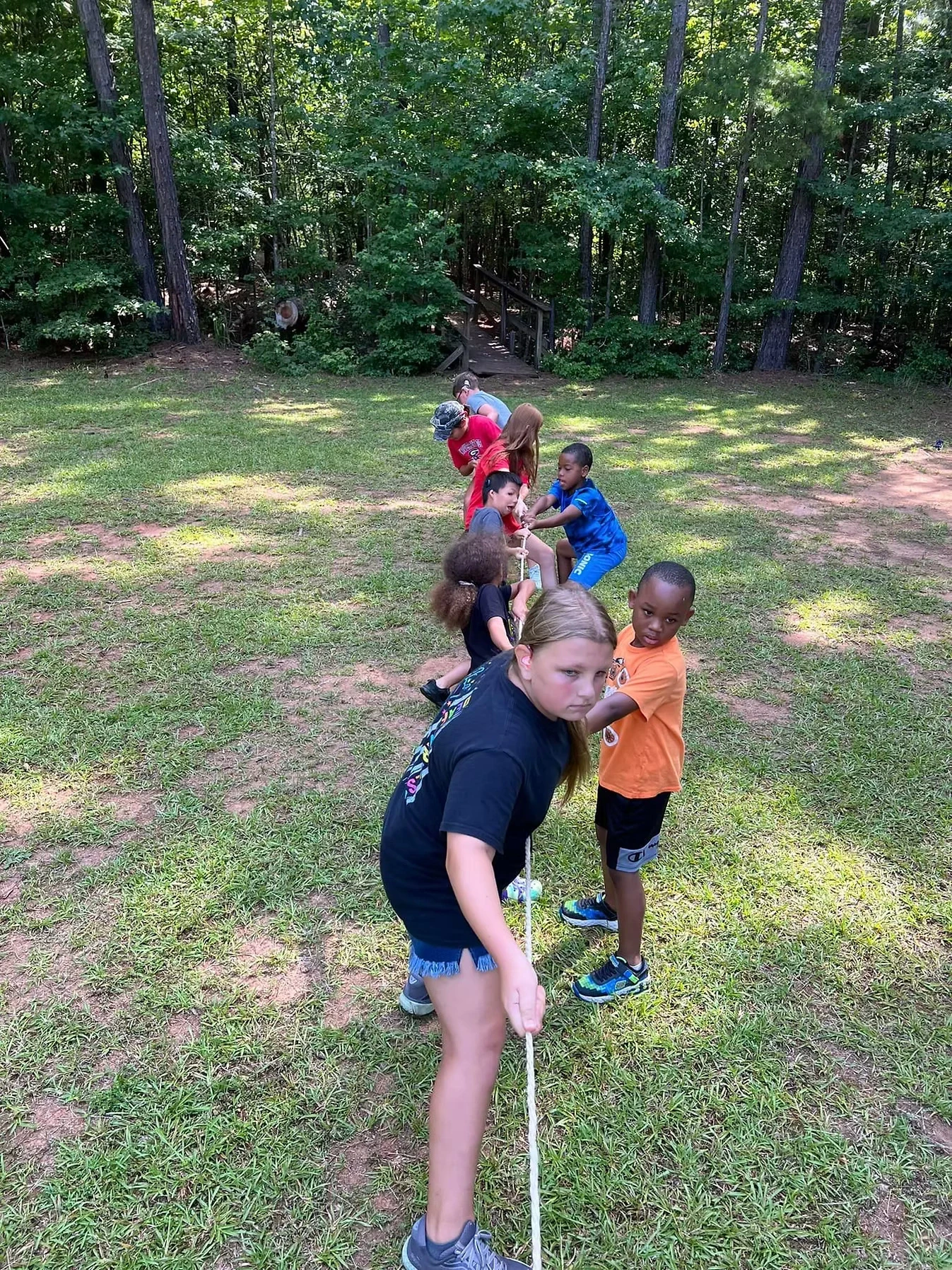 Campers playing tug-of-war outdoors on a grassy field.