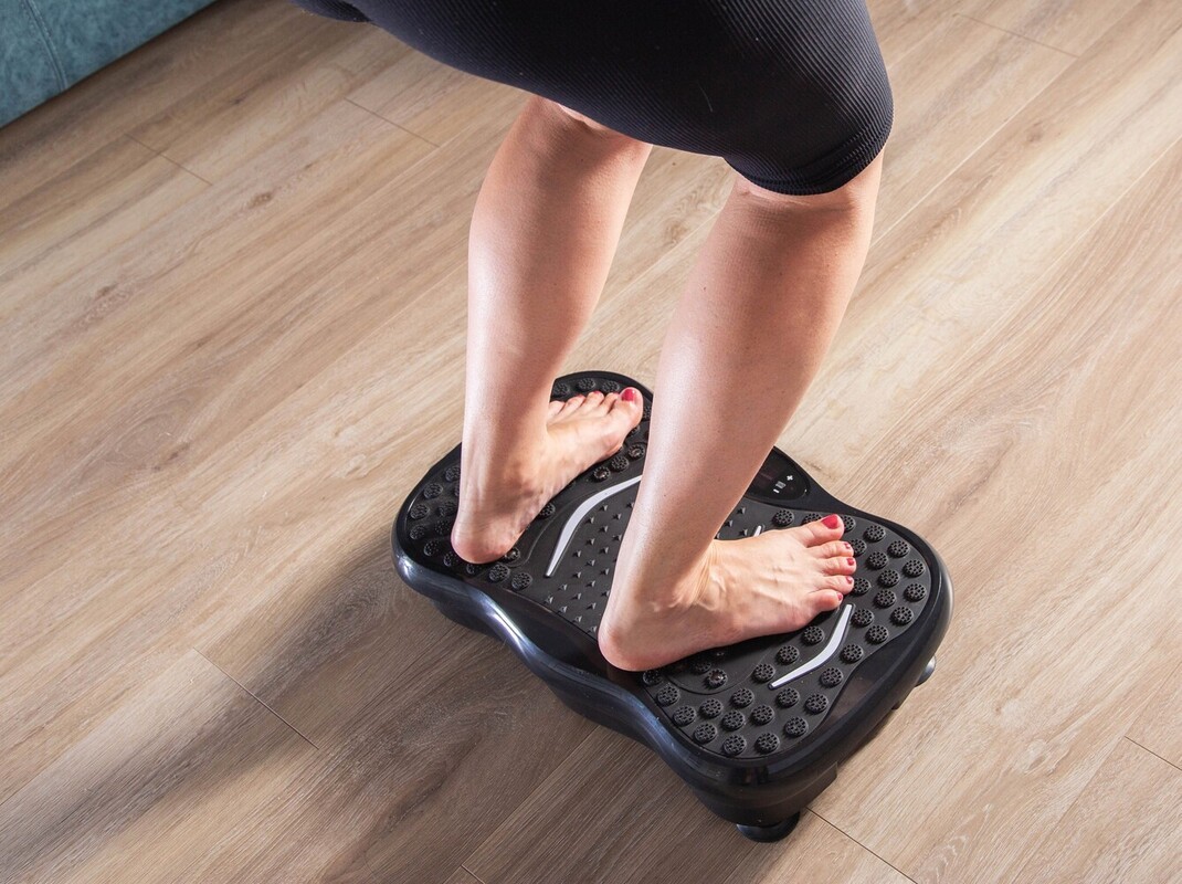 barefoot woman doing an easy workout on a weight loss vibration machine at home