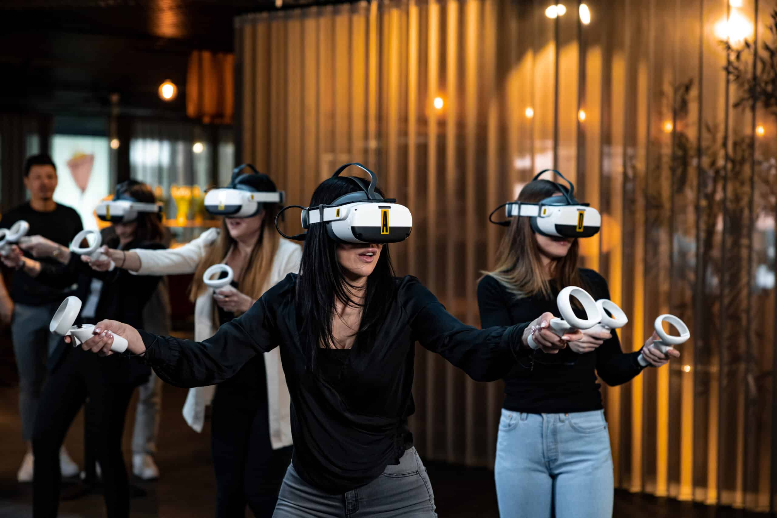 A young person with curly hair smiles at the camera while sitting in front of a laptop against a dark background.