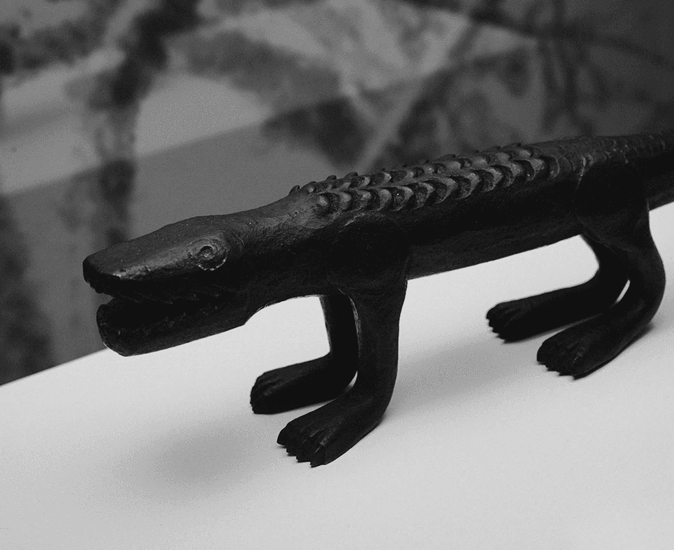 A minimalist, black-and-white product shot of an abstract bronze crocodile sculpture on a clean white surface. This highlights the studio’s expertise in museum art direction and the clean, Swiss-inspired presentation of historical artifacts.